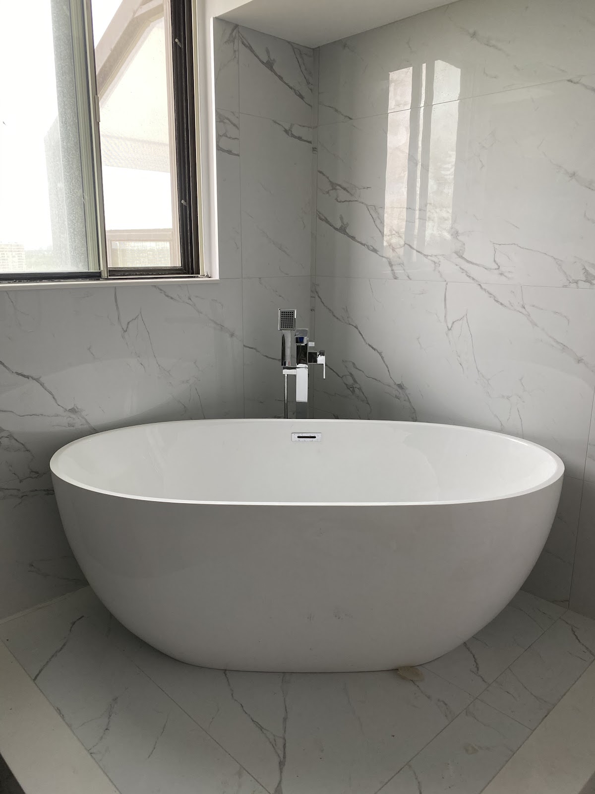 Freestanding soaker tub against marble-look tile in a finished bathroom