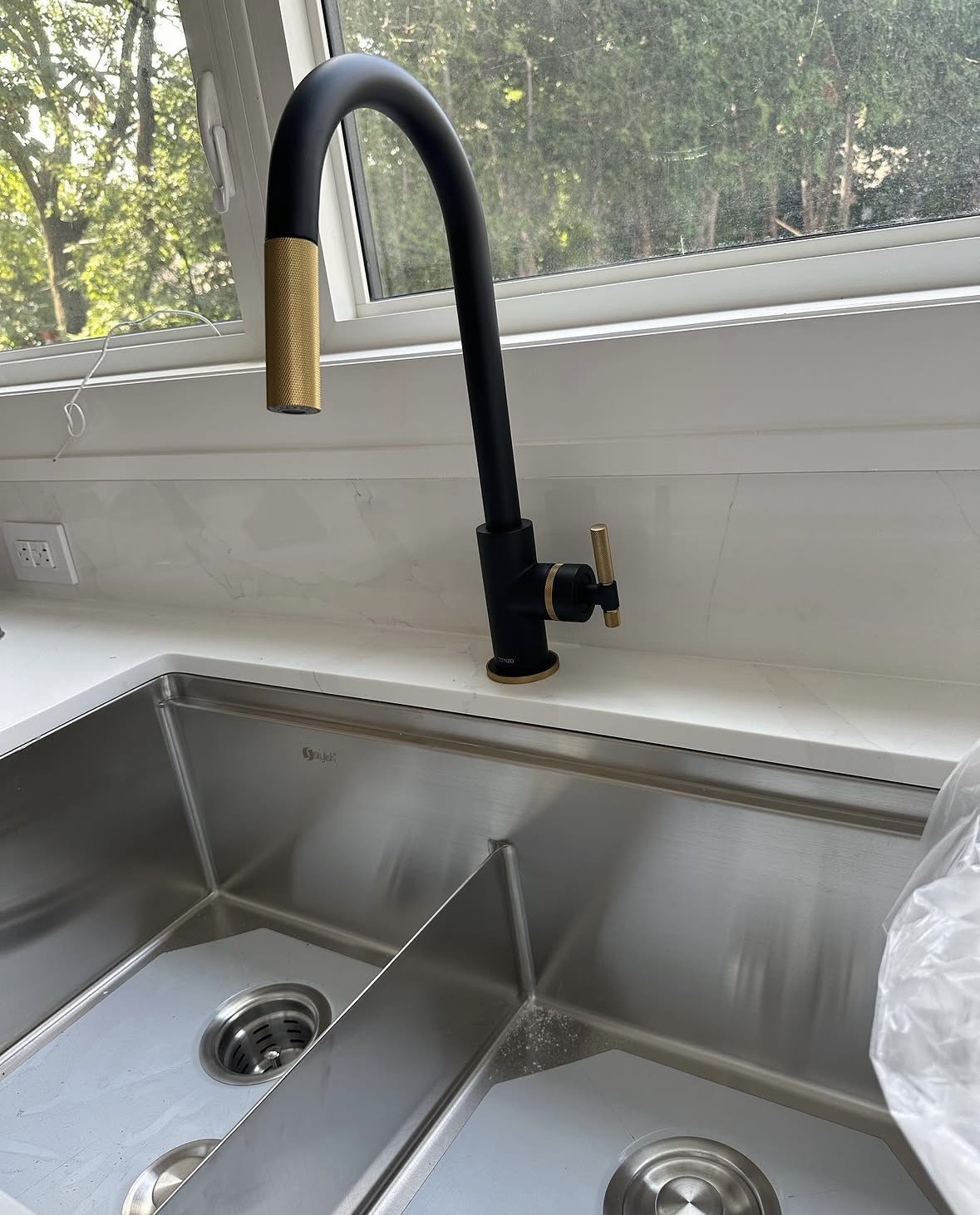 Matte black and brass kitchen faucet installed over a stainless double sink